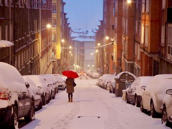 Rear view of man walking on snow covered road in city