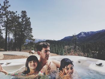 Father with daughters in swimming pool against sky