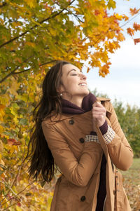 Woman wearing coat standing against trees in park during autumn