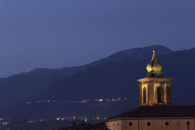 Illuminated building by mountains against clear blue sky