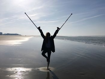 Silhouette arms raised woman with walking canes standing at beach