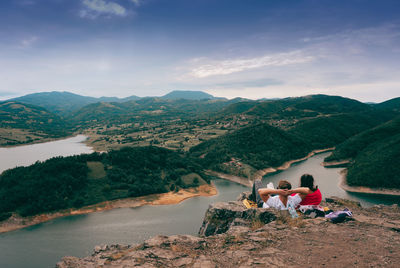 Couple sitting on mountain against sky