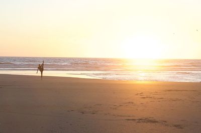 Silhouette teenage girl exercising at beach against sky during sunset