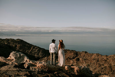 Rear view of people standing on rock by sea against sky