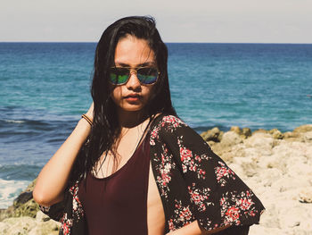 Portrait of beautiful young woman standing at beach against sky