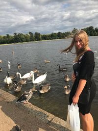 Portrait of young woman standing by birds in lake