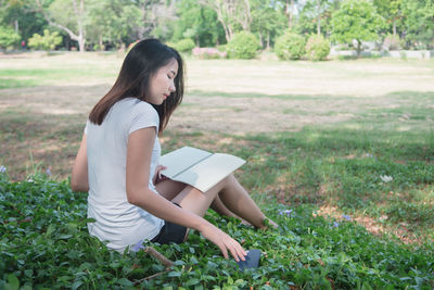 Young woman using phone while sitting on field