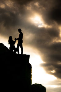 Low angle view of silhouette people on rock against sky during sunset