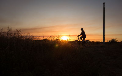 Silhouette teenage girl riding bicycle on land against sky during sunset