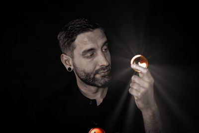 Portrait of man holding lit candle against black background