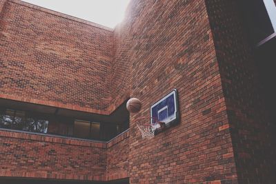 Low angle view of ball falling in basketball hoop attached on brick wall