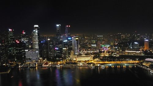 Illuminated city by river against clear sky at night