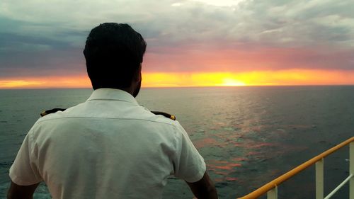 Rear view of male navy officer on boat in sea during sunset