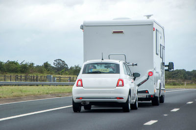 Vehicles on road against cloudy sky