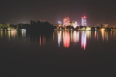 Illuminated buildings by river against sky at night