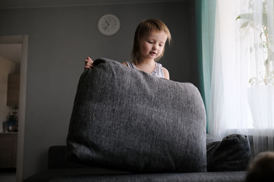 Kid toddler builds house from pillows on sofa in living room, lifestyle and games in real interior