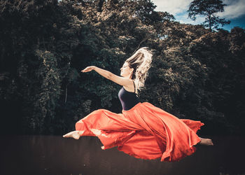 Young ballet dancer wearing red skirt while dancing in forest