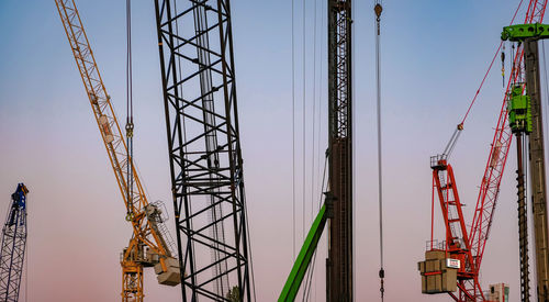 Low angle view of cranes against sky during sunset