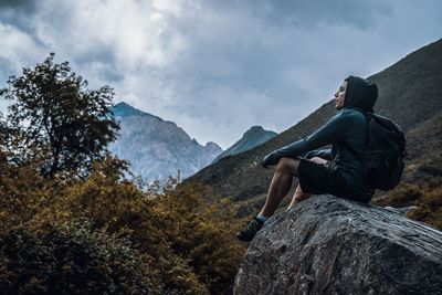 Man sitting on rock by mountains against sky