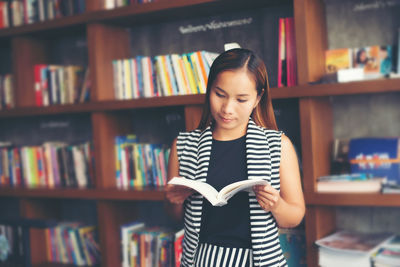 Woman reading book while standing at library