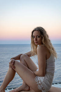 Portrait of woman sitting against sea at sunset
