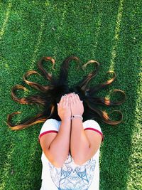 High angle view of woman covering face with hands while lying down on field