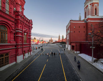 People walking on street amidst buildings against blue sky during winter