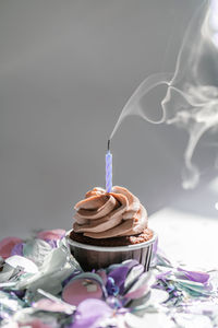 A cupcake with a candle stands on a white background with a shadow.