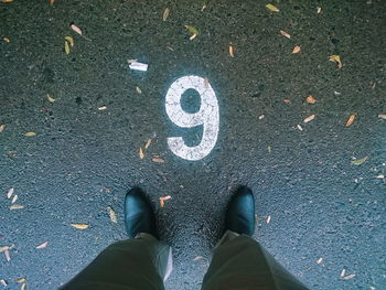 Low section of man standing by number 9 on wet road