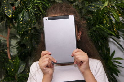 Midsection of person holding mobile phone while standing by tree