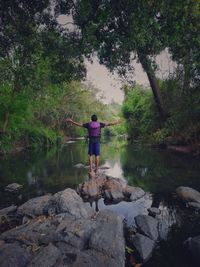 Rear view of man standing on rock by lake