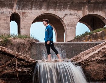 Side view of man standing on arch bridge