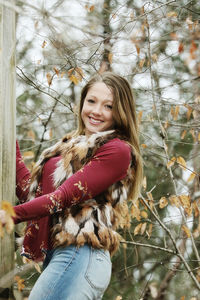 Portrait of happy teenage girl standing by tree trunk