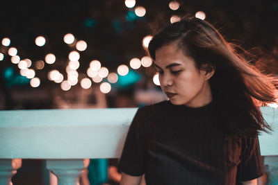 Portrait of beautiful woman standing by illuminated lights at night