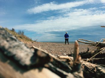 Rear view of young woman standing at beach against sky