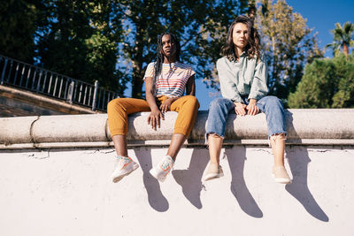 Low angle view of friends sitting on retaining wall