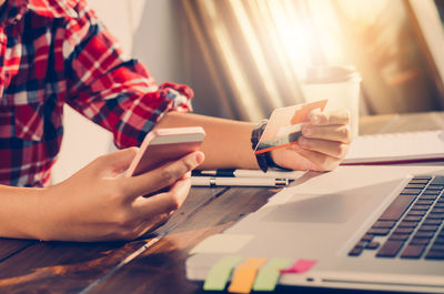 Midsection of woman holding credit card while using laptop at table