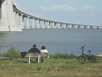 Rear view of couple sitting on bench at tagus riverbank