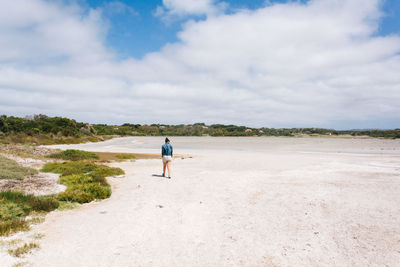 Rear view of woman walking on beach against sky