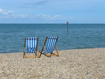 Chairs on beach against blue sky