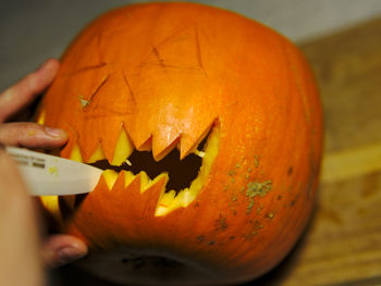 Close-up of hand holding pumpkin against orange background