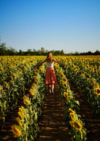 Rear view of woman walking on field against clear sky