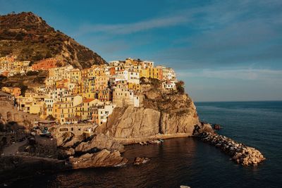 Buildings on mountain by sea against sky during sunset