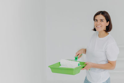 Portrait of smiling woman holding paint standing against wall