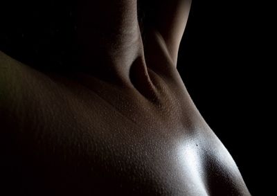 Midsection of topless woman against black background