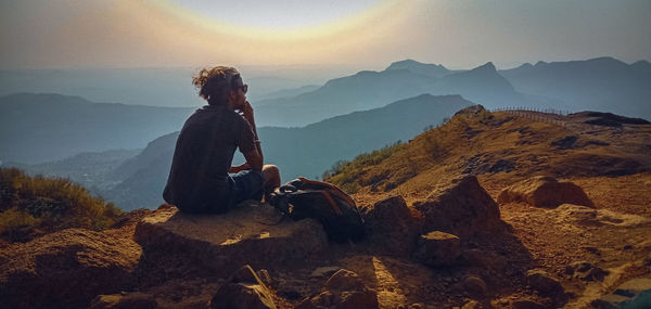 Man sitting on rock looking at mountains against sky