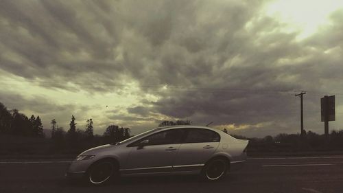 Cars on road against cloudy sky