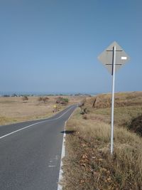 Road sign on field against clear blue sky