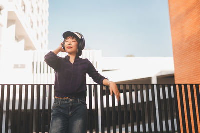 Mid adult woman standing by railing against sky