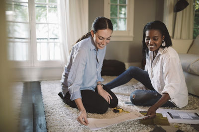 Smiling female designers discussing while sitting on carpet at home office